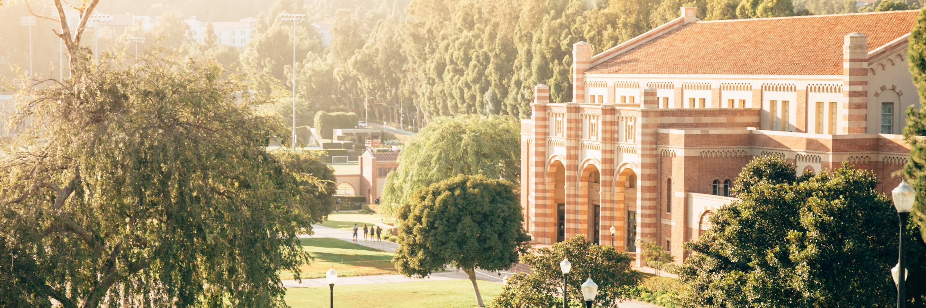 Kaufman Hall at UCLA is surrounded by lush trees and sunlight on a bright, peaceful day.
